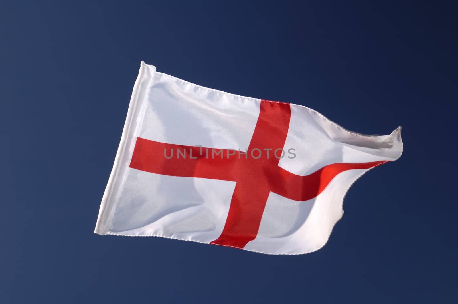 The cross of St George, the flag of England, isolated against a clear blue sky. Motion blur at the tip of the flag.