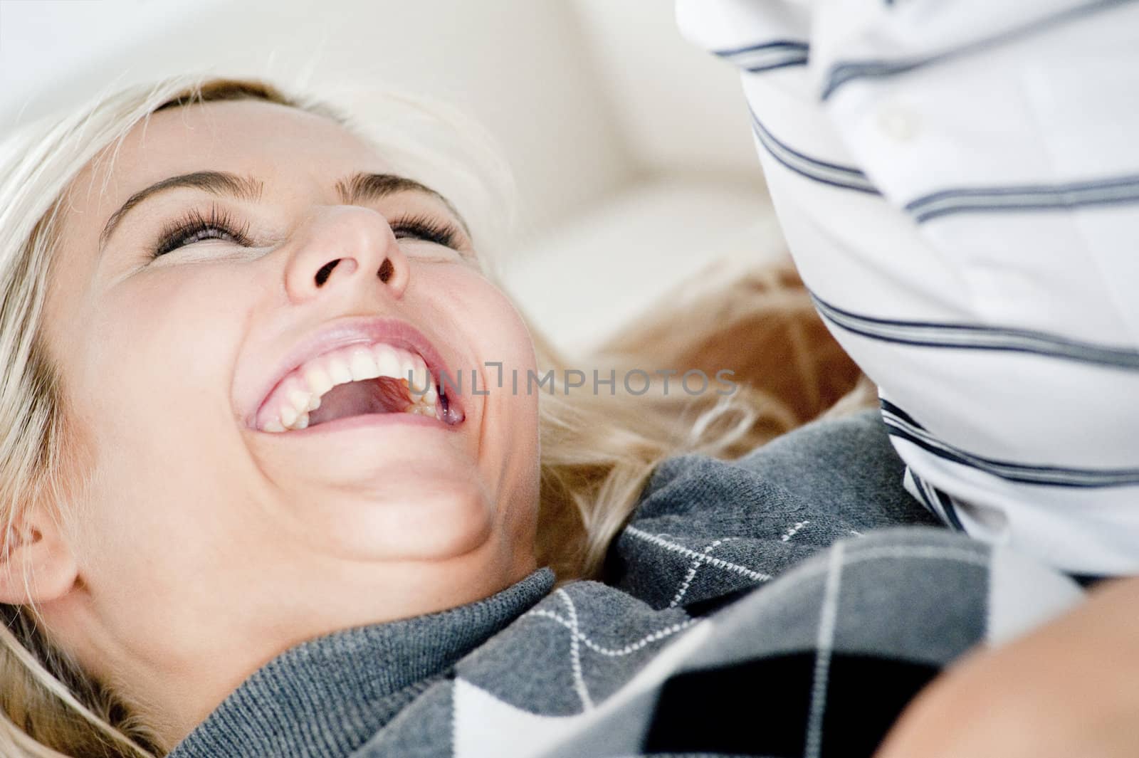 Cropped close-up of woman laughing as she reclines in her partner's lap. Horizontal format.