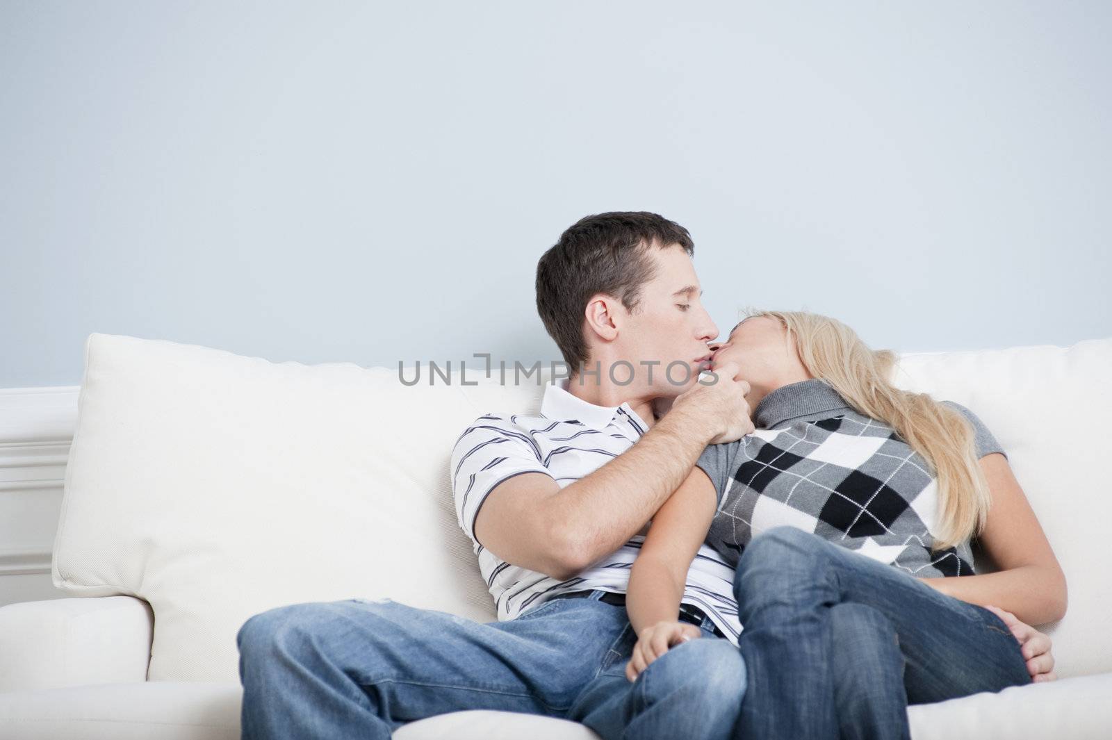 Cropped view of couple sitting on white couch and kissing. Horizontal format.