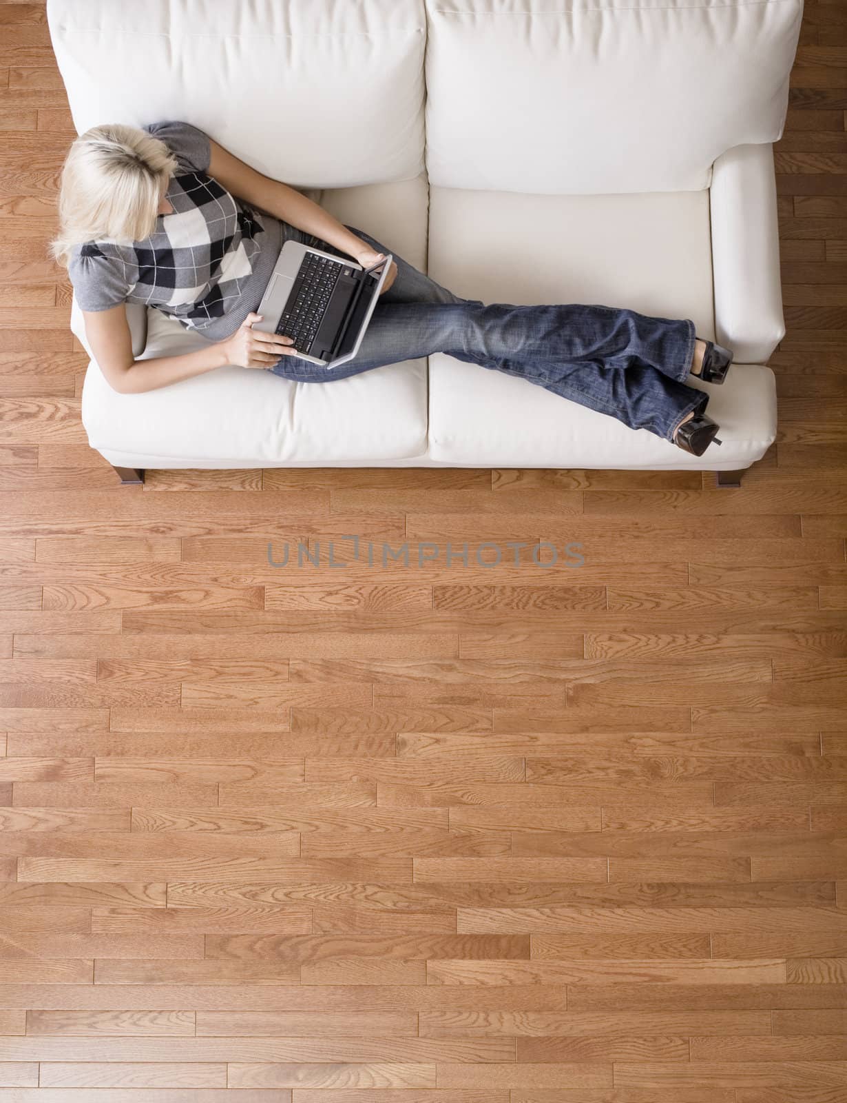 Full length overhead view of woman reclining on white couch and using a laptop. Vertical format.