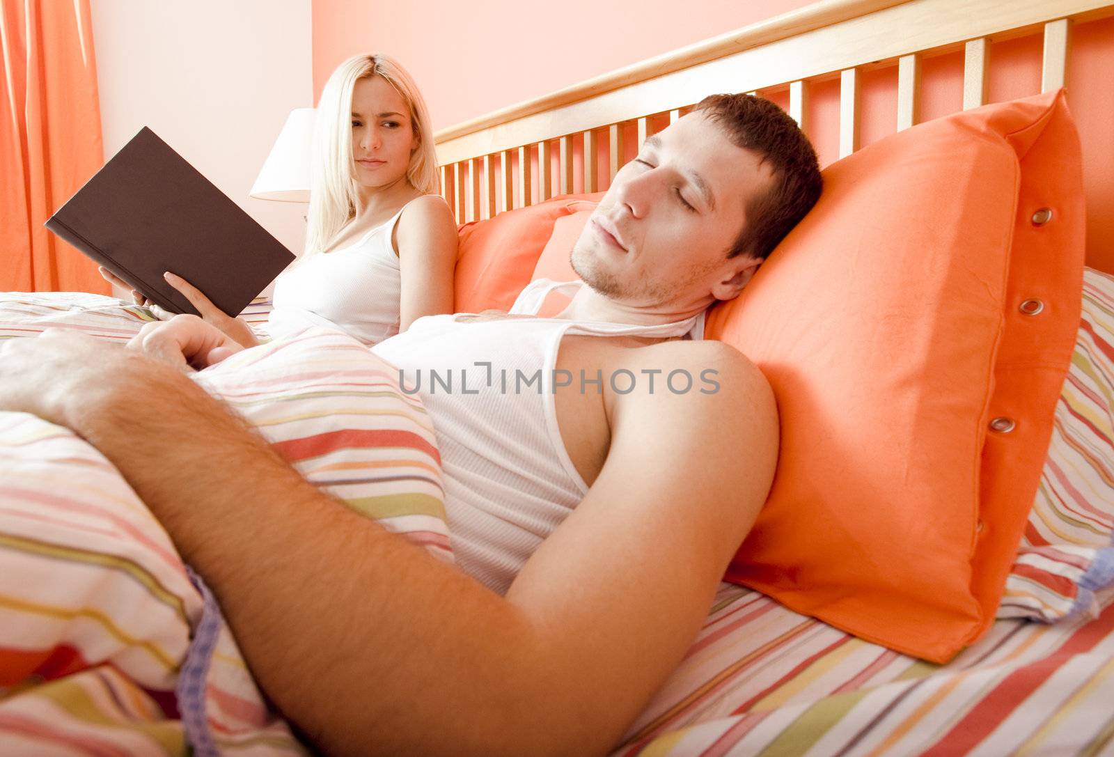 Woman holds book and watches man sleeping next to her. Horizontal format.
