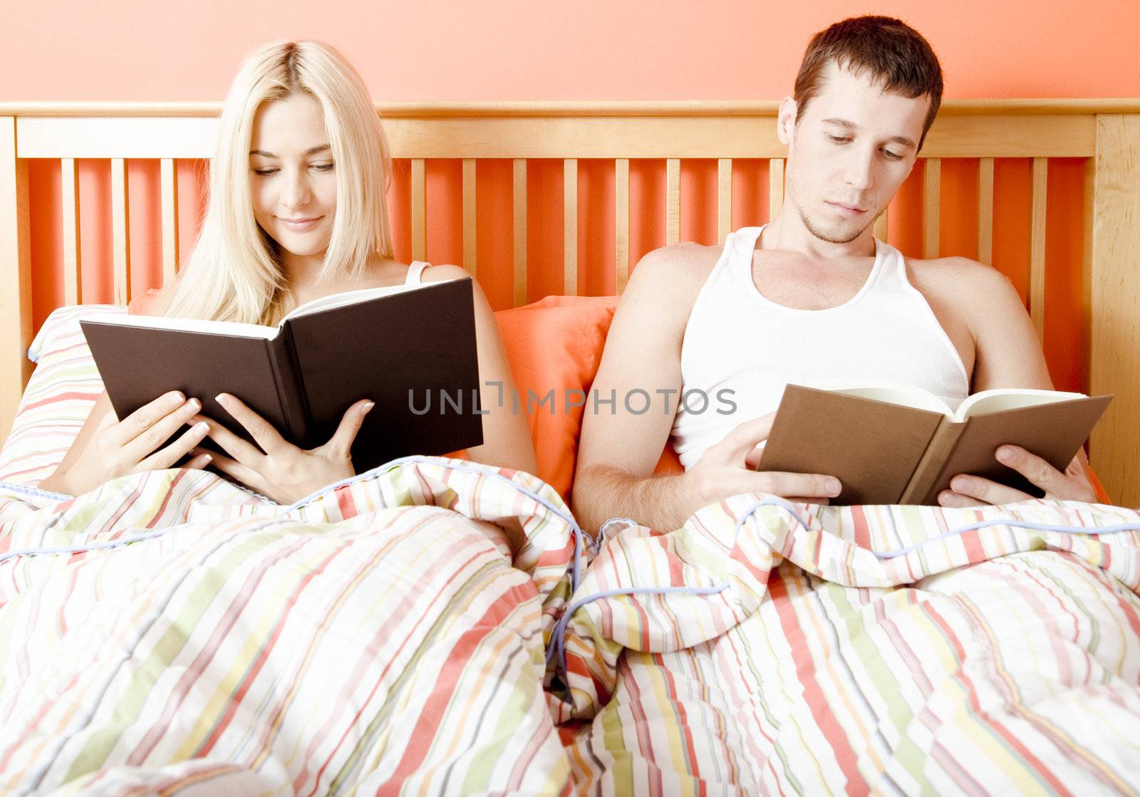Man and woman reading side-by-side in bed. Horizontal format.