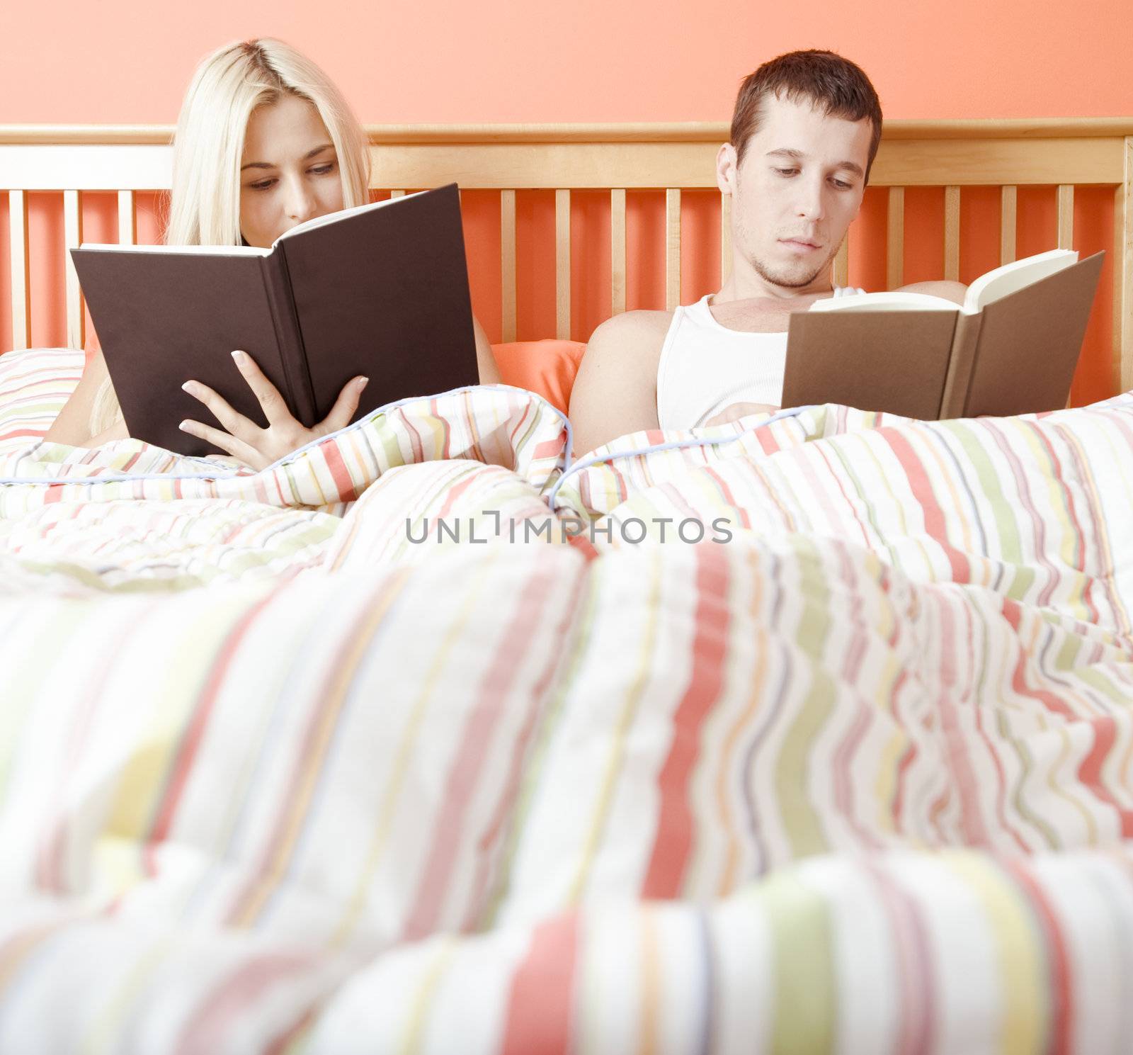 Man and woman reading side-by-side in bed. Square format.