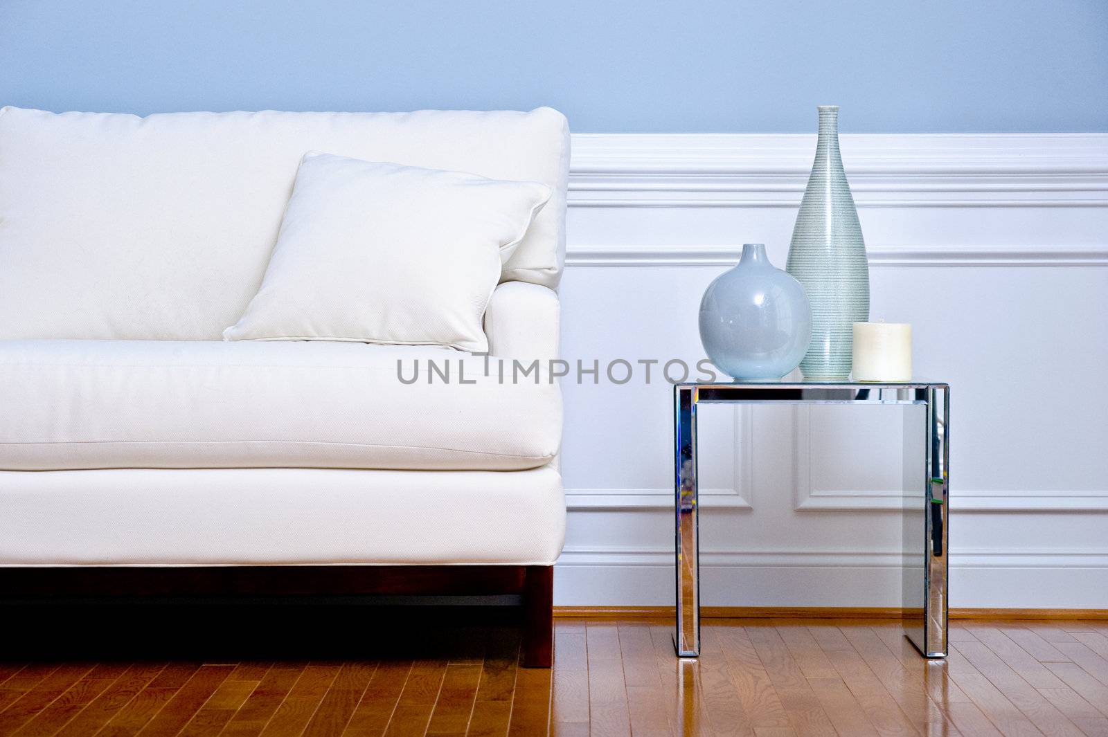 Cropped view of white couch and side table with vases, in a living room with a wood floor. Horizontal format.