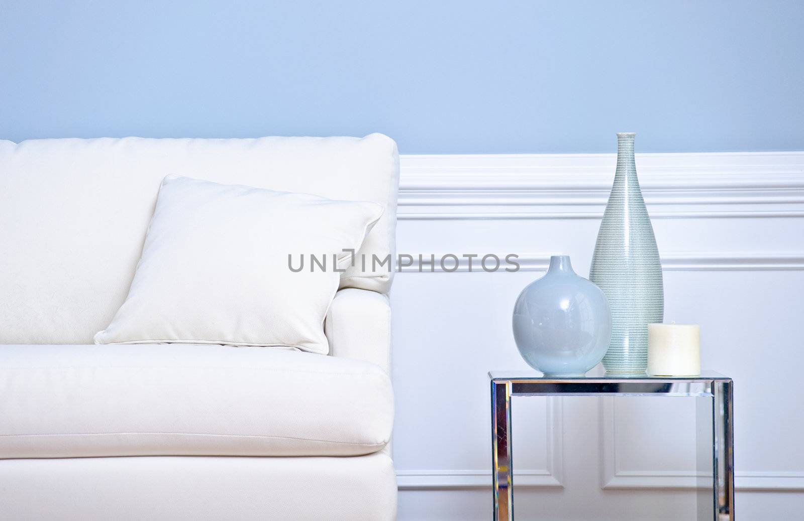 Cropped view of a living room, focusing on a white couch and side table with vases. Horizontal format.