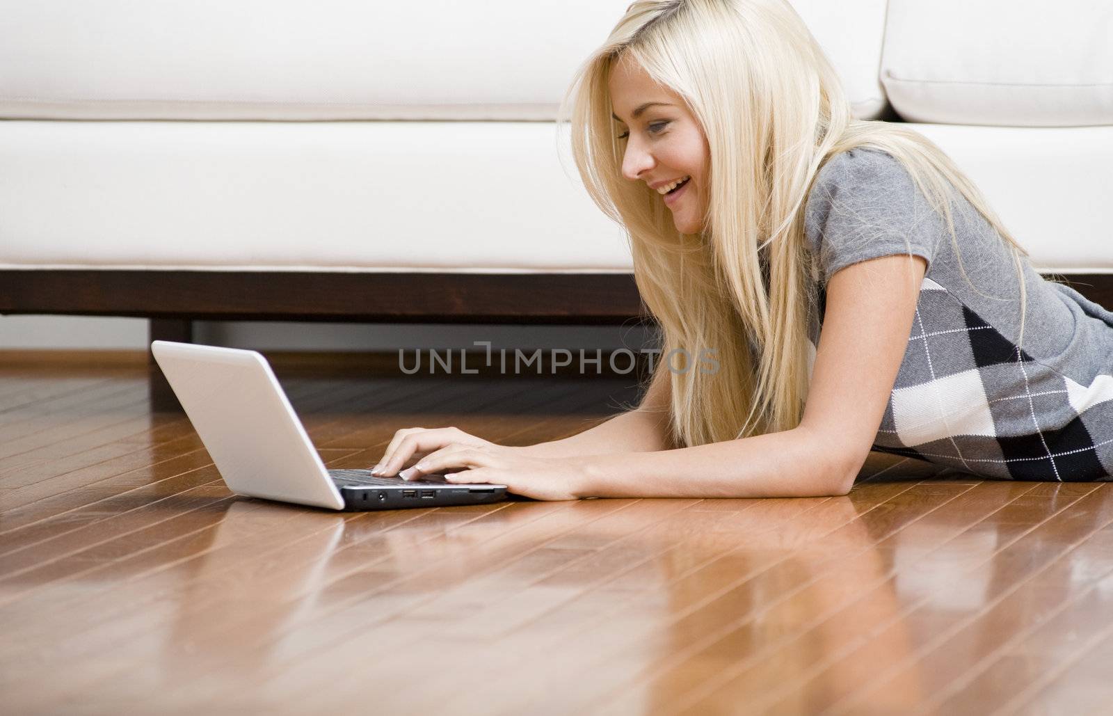 Smiling woman stretches out on the living room floor with her laptop. Horizontal format.
