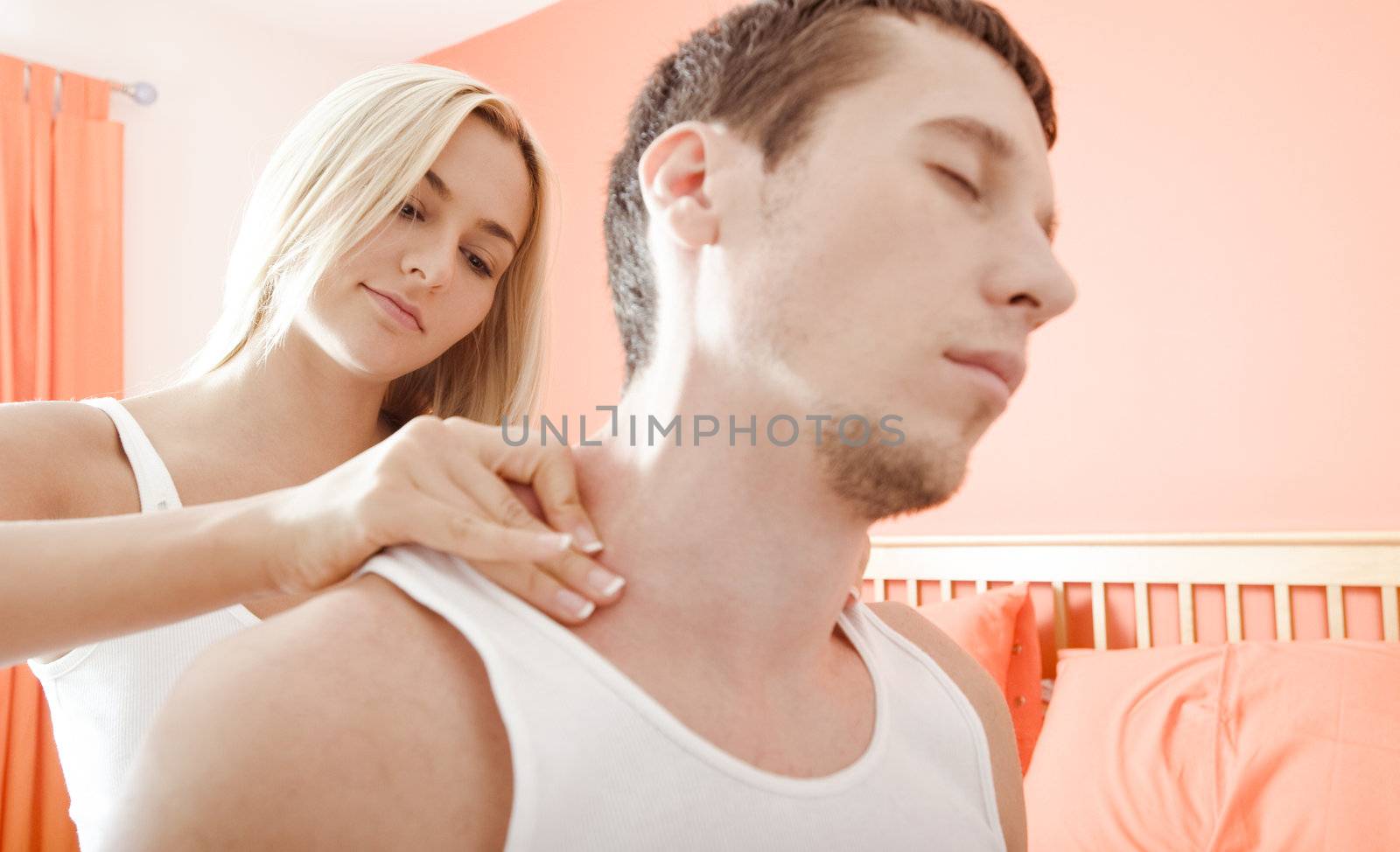Man and woman sit on bed as woman massages man's shoulders. Horizontal format.