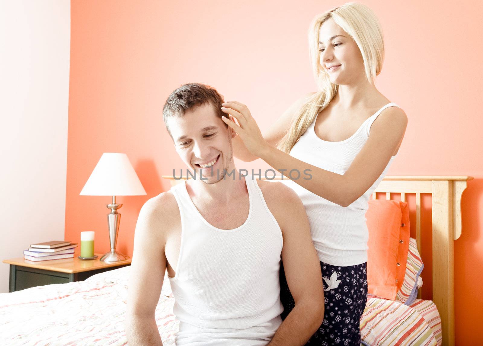 Woman ruffles man's hair as they relax in their bedroom. Horizontal format.
