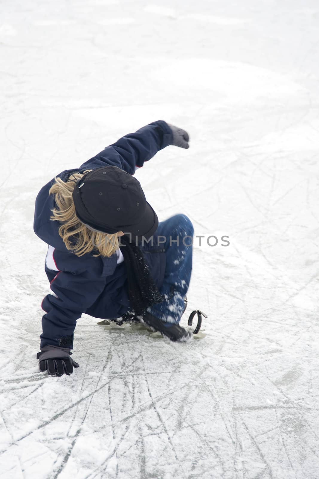 a young boy is falling on the ice, and loosing his ice-skate