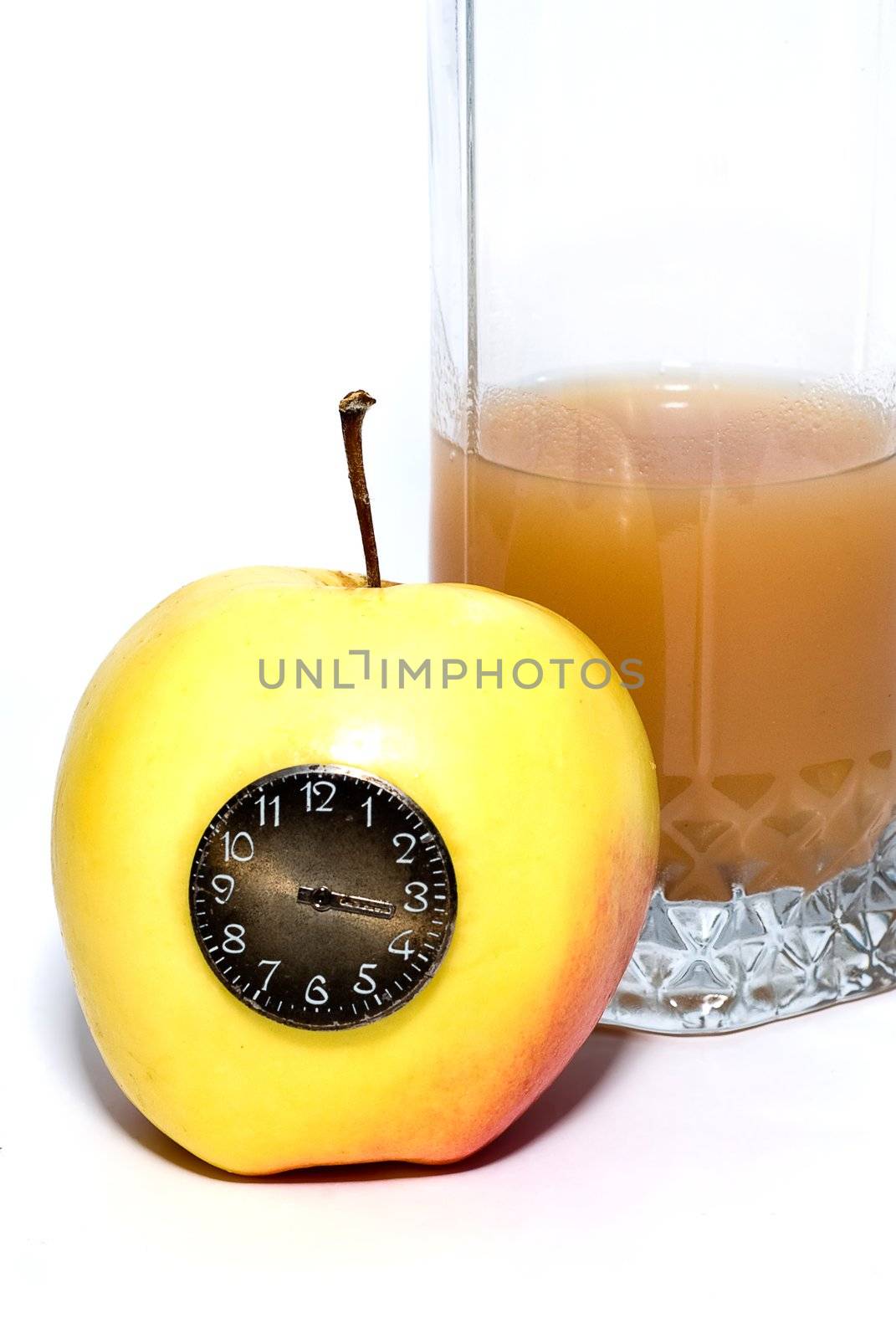 glass of juice behind the yellow apple with the clock