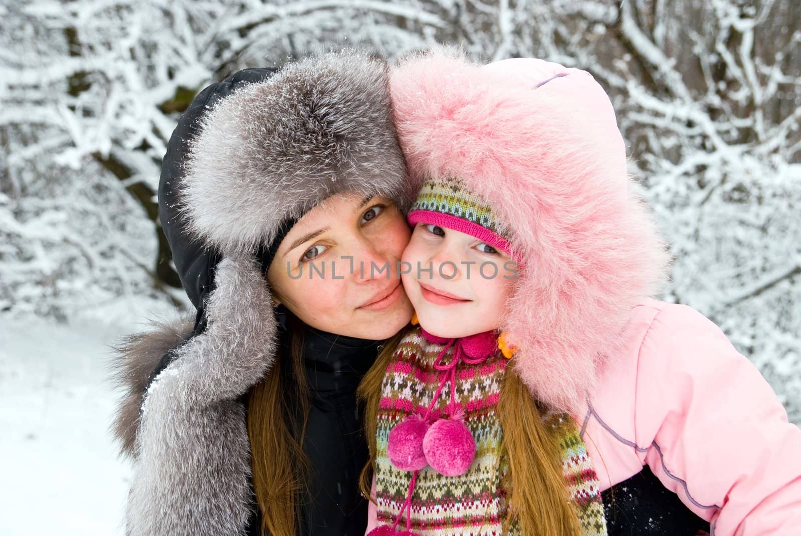 young mother and daugther in winter clothing hugging in a winter woods