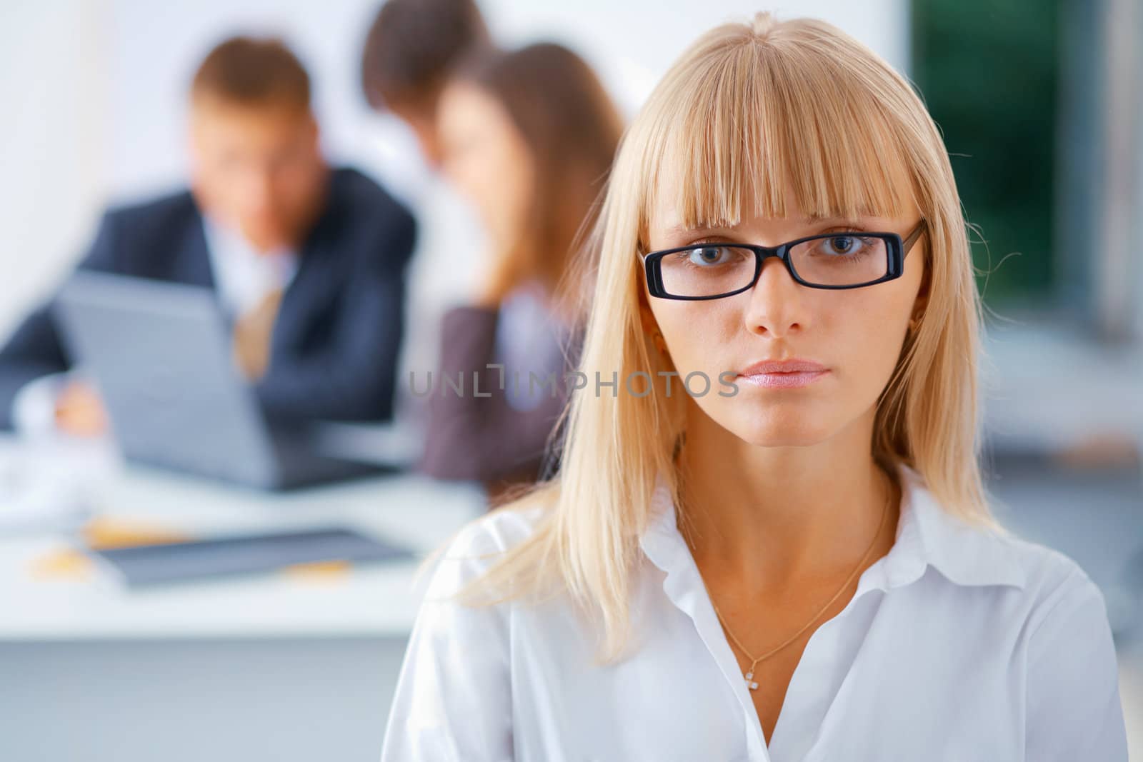 Portrait of young serious business woman with her working colleagues at the background