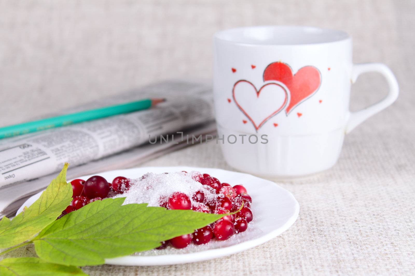 Cowberry in sugar against a mug with hearts and the newspaper removed close up