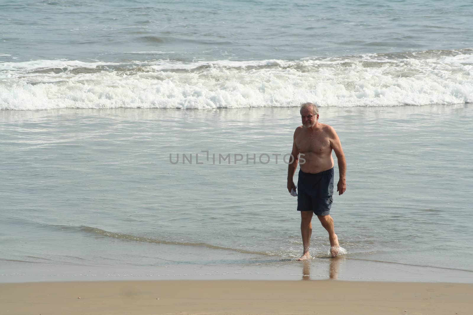 Elderly man walking on beach in the waves