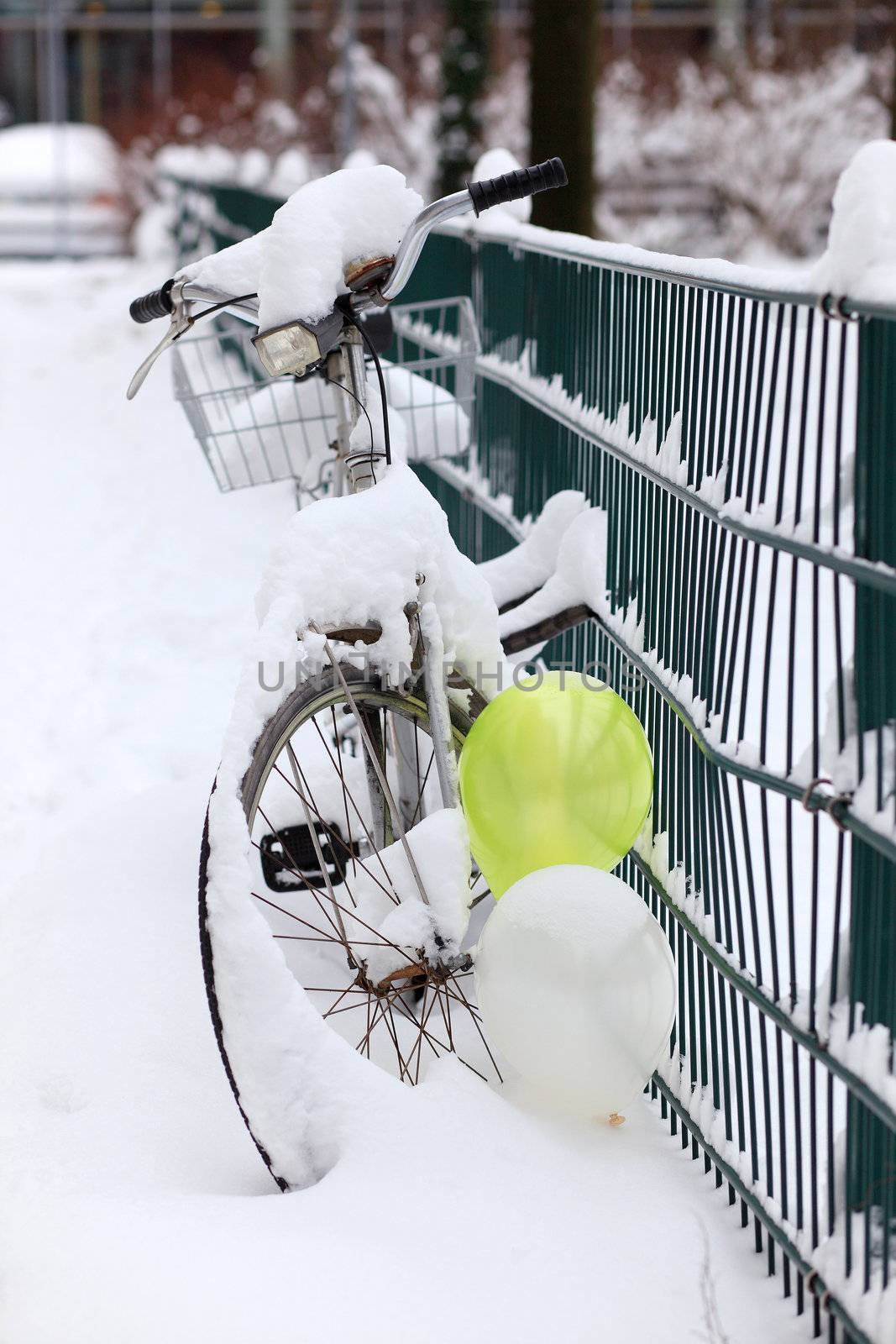 a bike covered with a lot of snow, standing at a fence, decorated with balloons