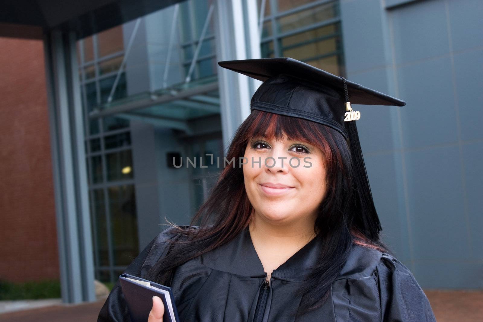 A recent graduate posing in her cap and gown and holding her fresh diploma or degree.