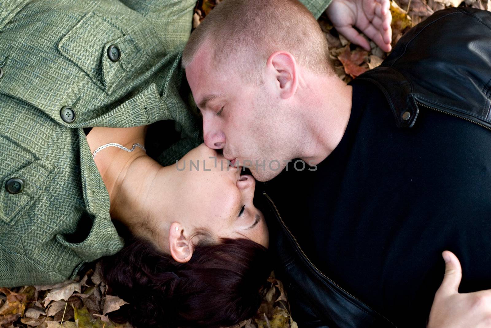 A young happy couple passionately kissing each other while laying in some autumn leaves.