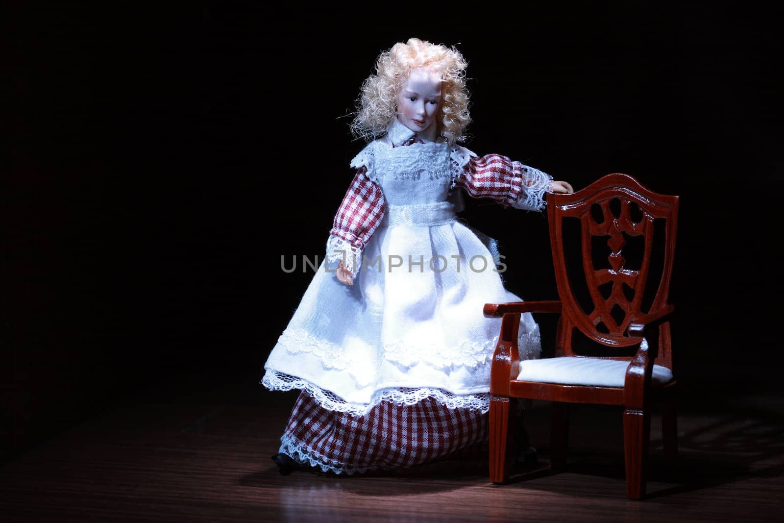 Nice miniature German souvenir doll standing near small chair on dark background