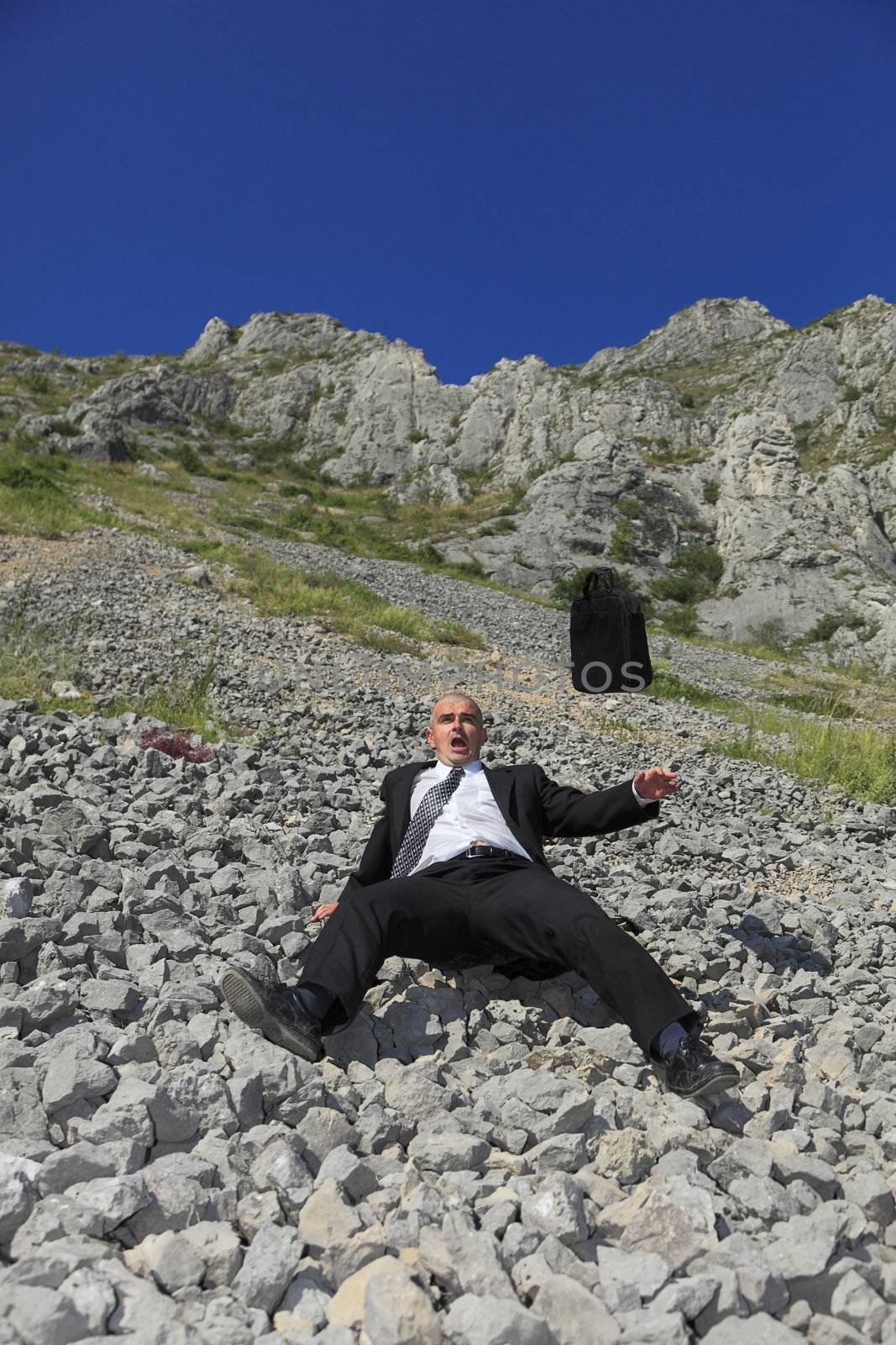 Image of a businessman in a difficult situation sliding on a rocky mountain slope.