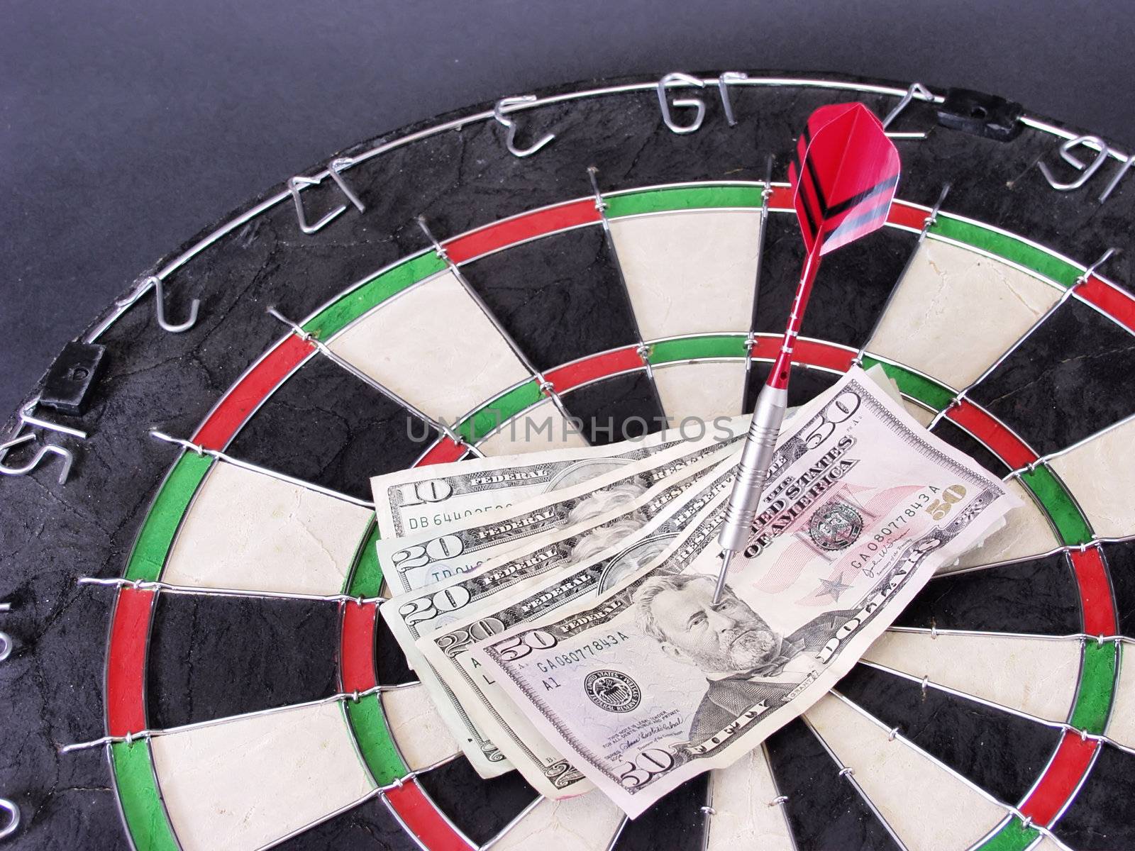 One Hundred US Dollars pinned by a dart on a steel tip dart board.