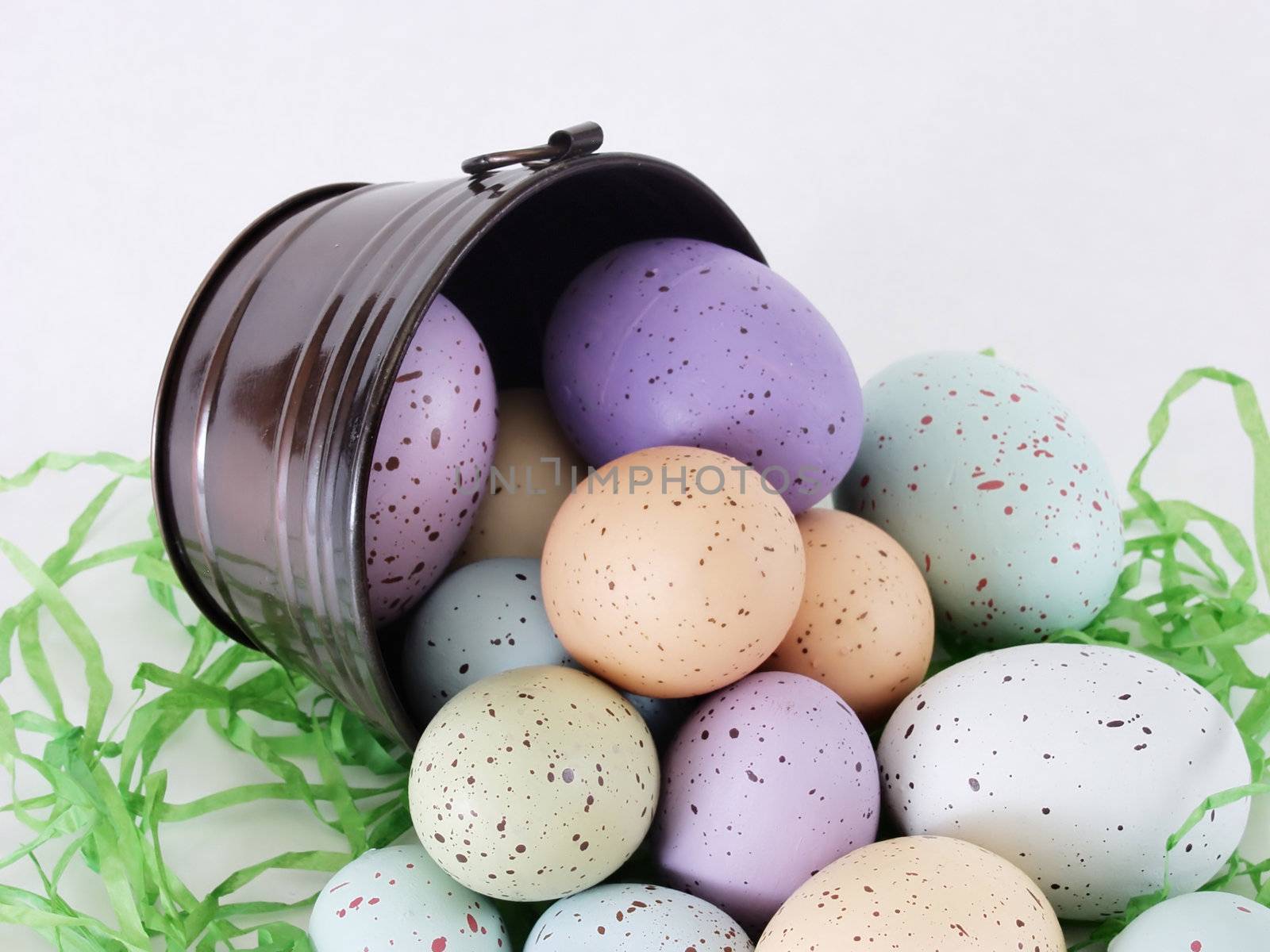 Colorful Easter Eggs in pastels tipped out of a little black metal bucket, on green Easter grass