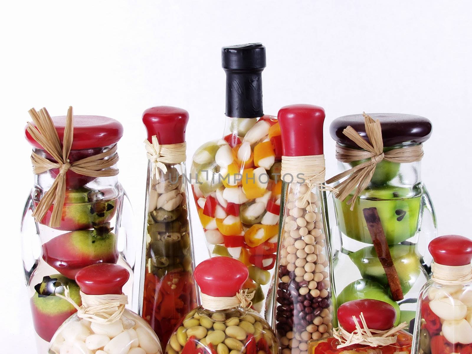 A colorful assortment of pickled spices in different shaped jars on white.