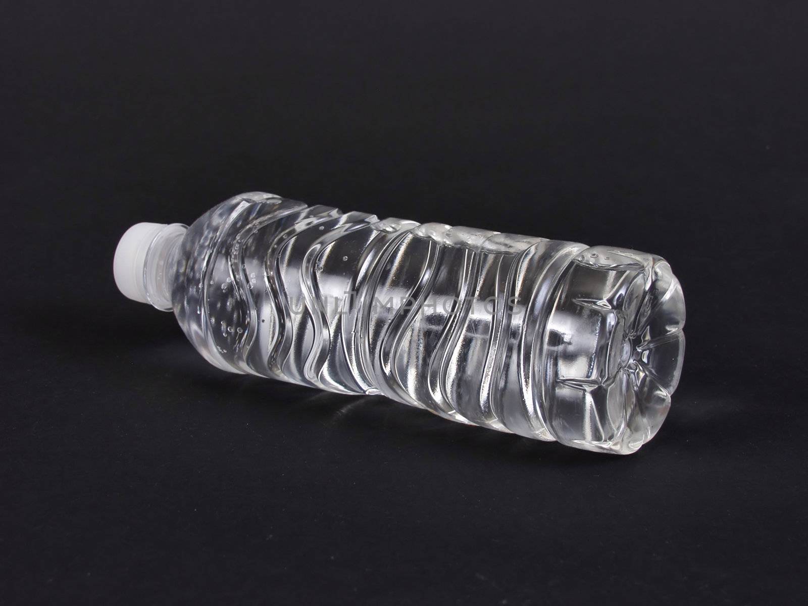 A full clear plastic water bottle laying on its side. Over a black background.
