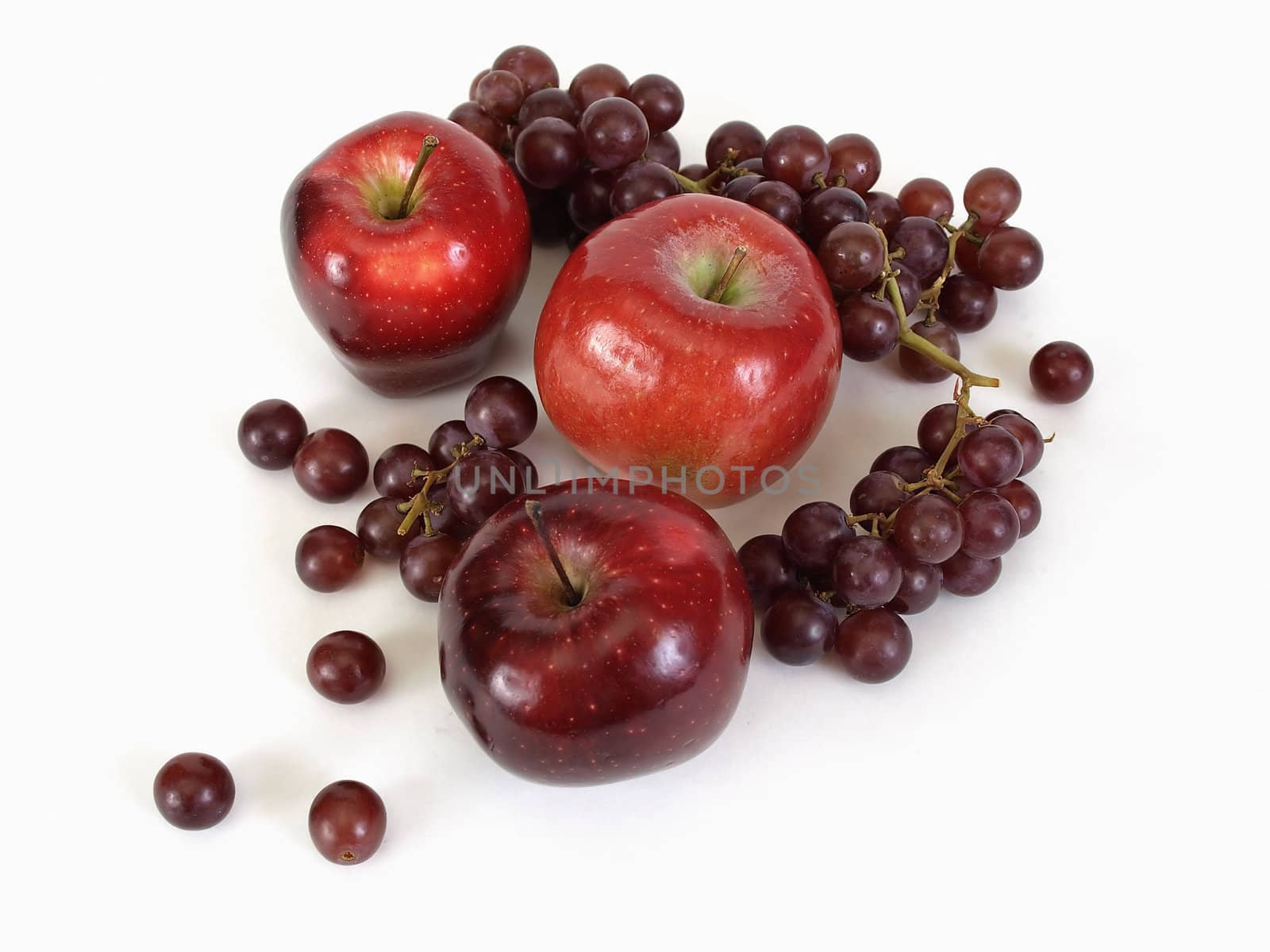 A group of three red apples and a bunch of grapes loose on a white background.