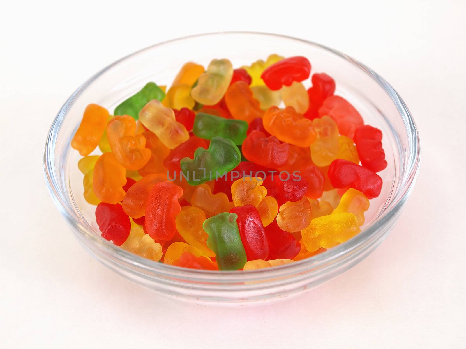 A small candy dish full of brightly colored candy bears. Over a white background.