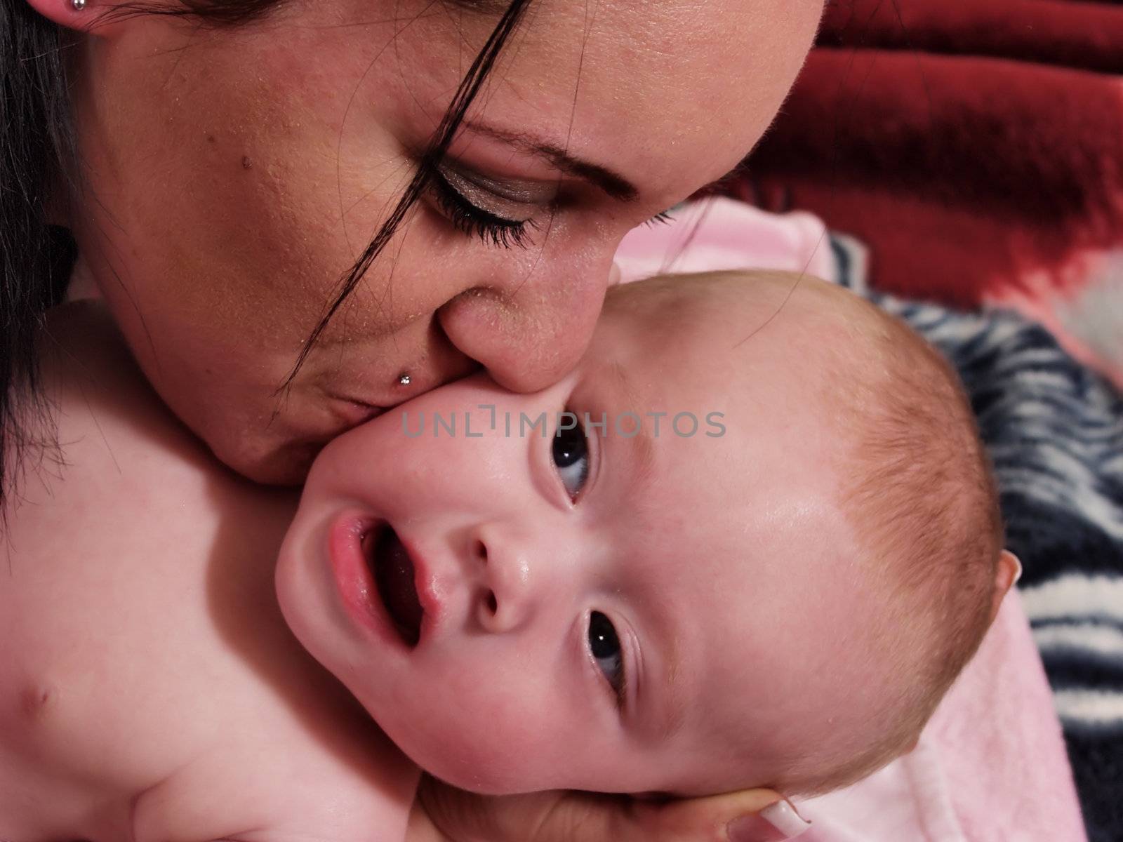 A mother with a pierced lip gives a protesting baby a kiss on the cheek.