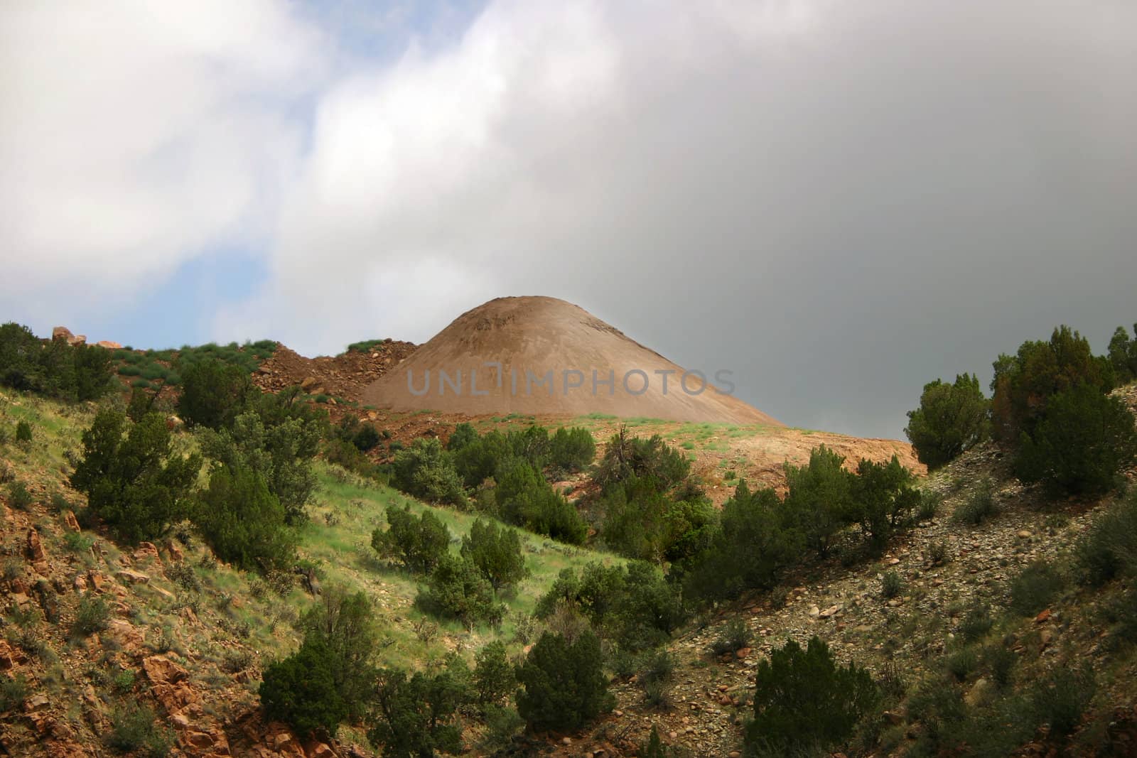 Mine tailings look like a cone of sand in a remote mountain landscape in the Colorado Rocky Mountains.