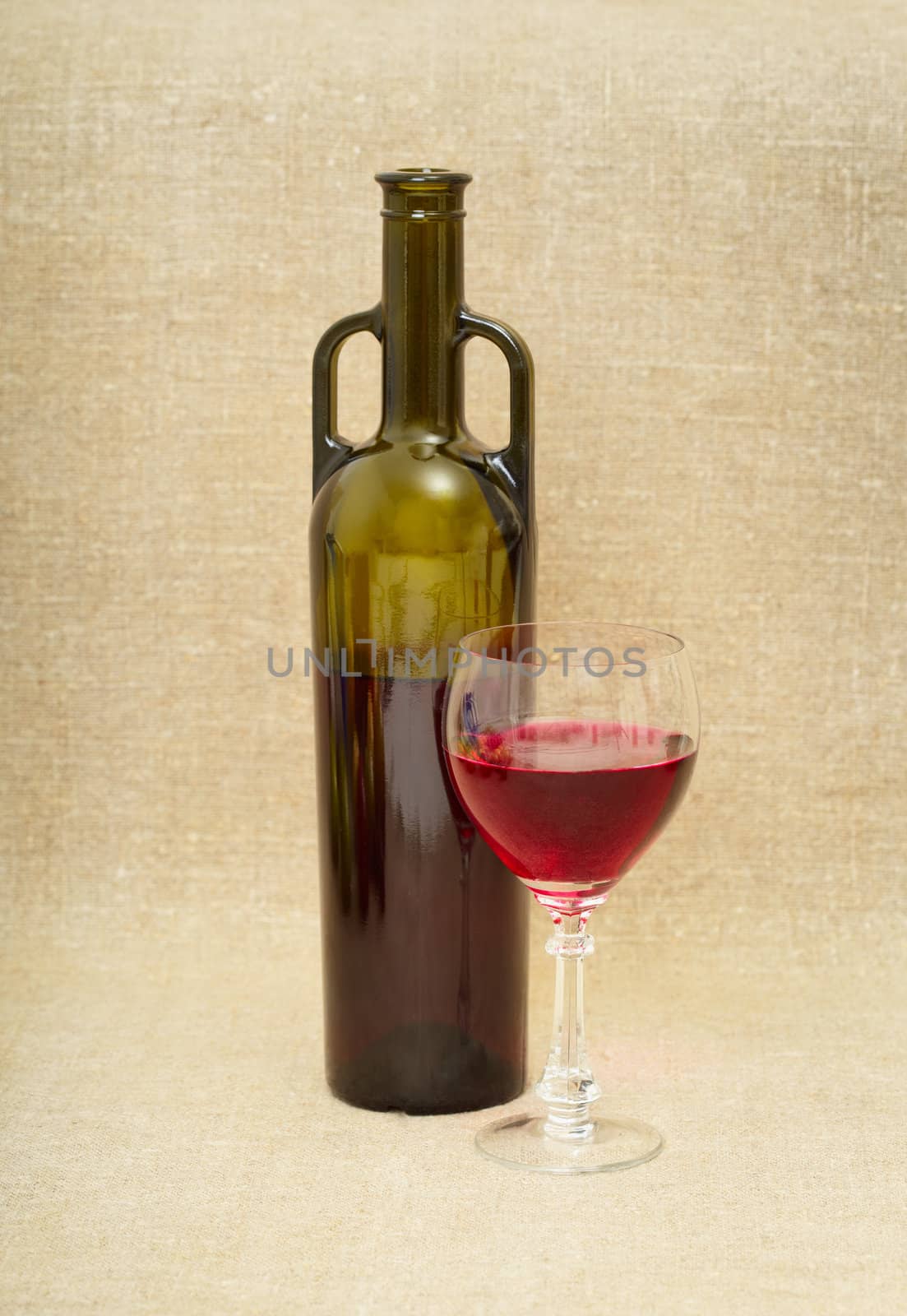 Bottle and glass with red wine against a canvas
