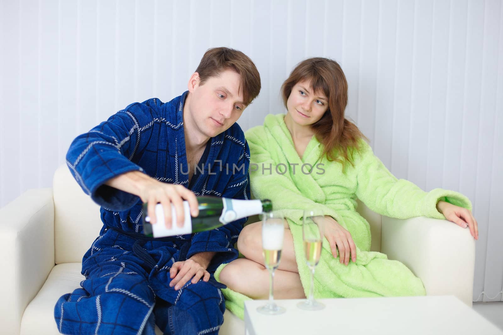 The man treats the lady with champagne, at home on a sofa