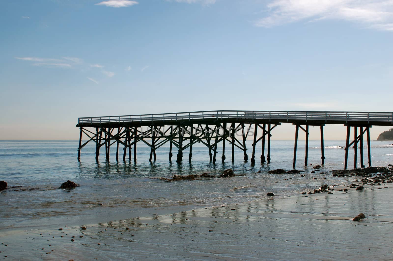 From right to left view of a rickety wooden pier/ jetty into the Pacific Ocean at Paradise Cove, California, with half sky, half sand with the pier/ jetty in the middle of the shot