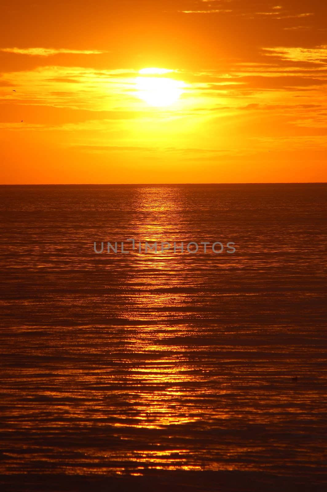 Orange sunset over Pacific Ocean in California, with the major part of the shot showing the reflection of the sun in the ocean