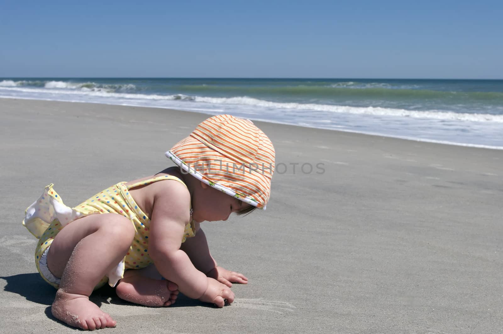 A baby plays with the sand during her first visit to the beach.