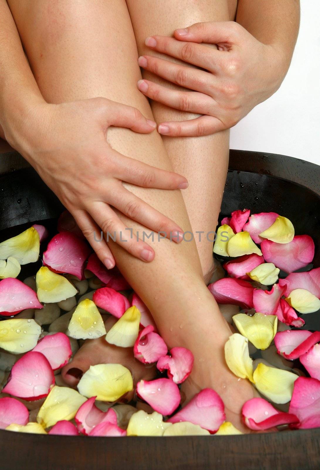 A woman luxuriates her weary feet with a relaxing footsoak.  Pink and yellow flower petals float on the warm water releasing a heavenly scent.