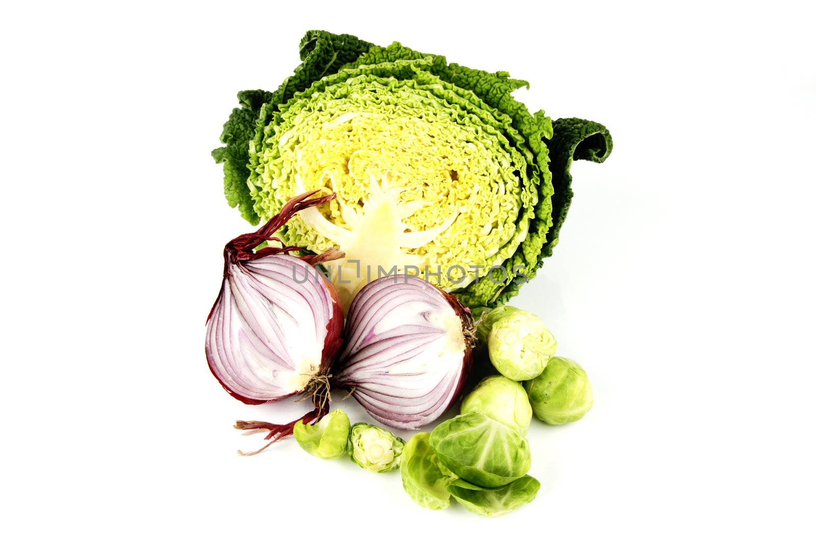 Half a raw green cabbage with a red onion cut in half and peeled sprouts on a reflective white background
