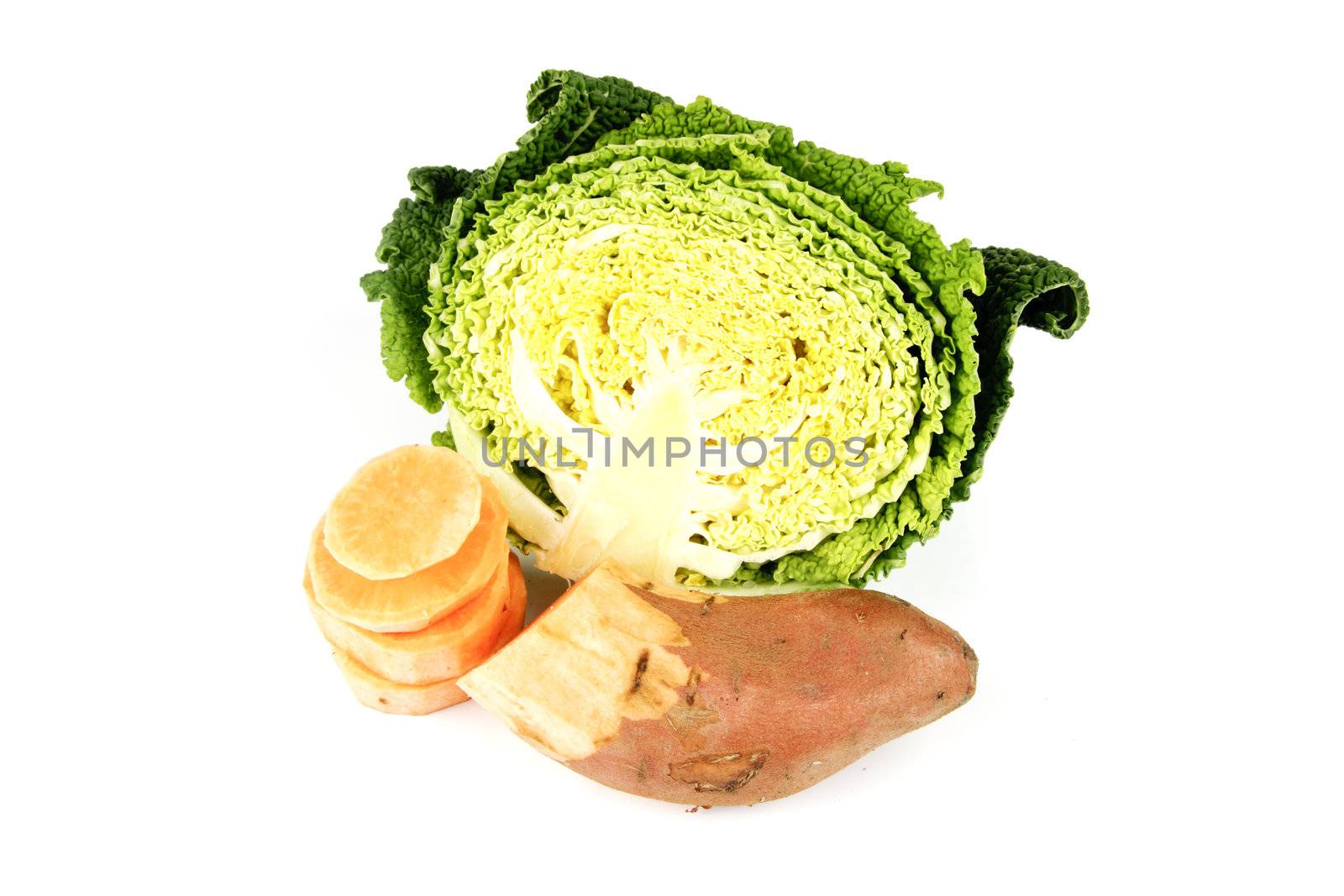 Half a raw green cabbage with half a sweet potato and slices on a reflective white background