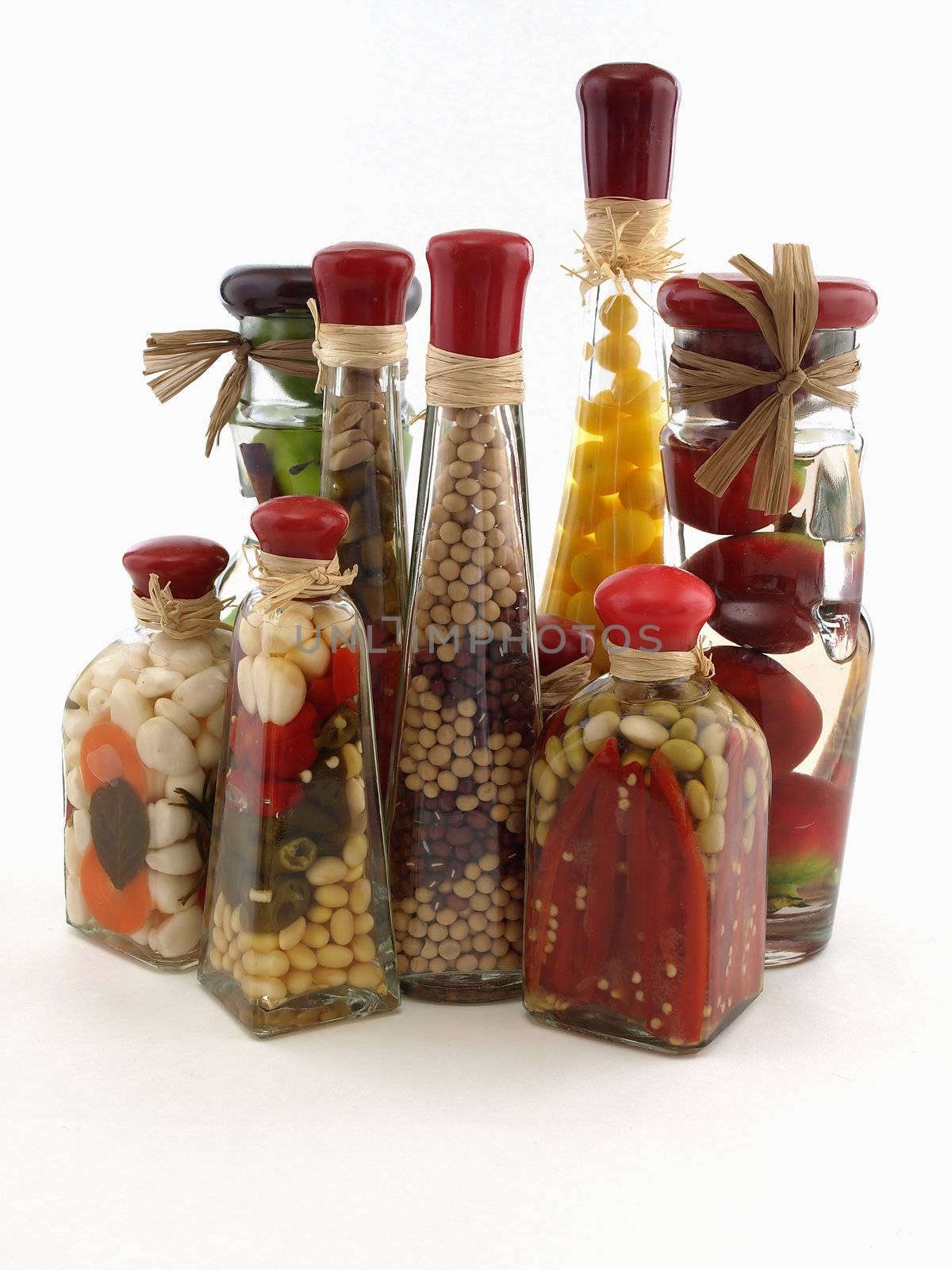 A colorful assortment of pickled spices in different shaped jars on white.