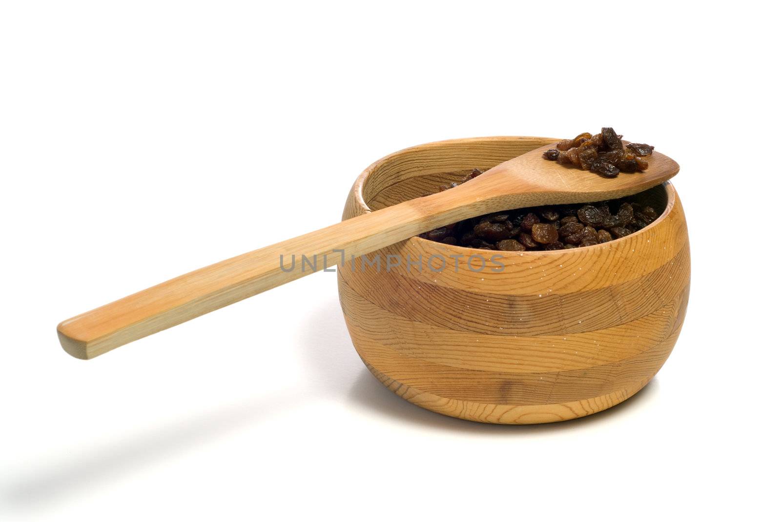 A wooden bowl of raisins with a wooden spoon resting on top, shot on white