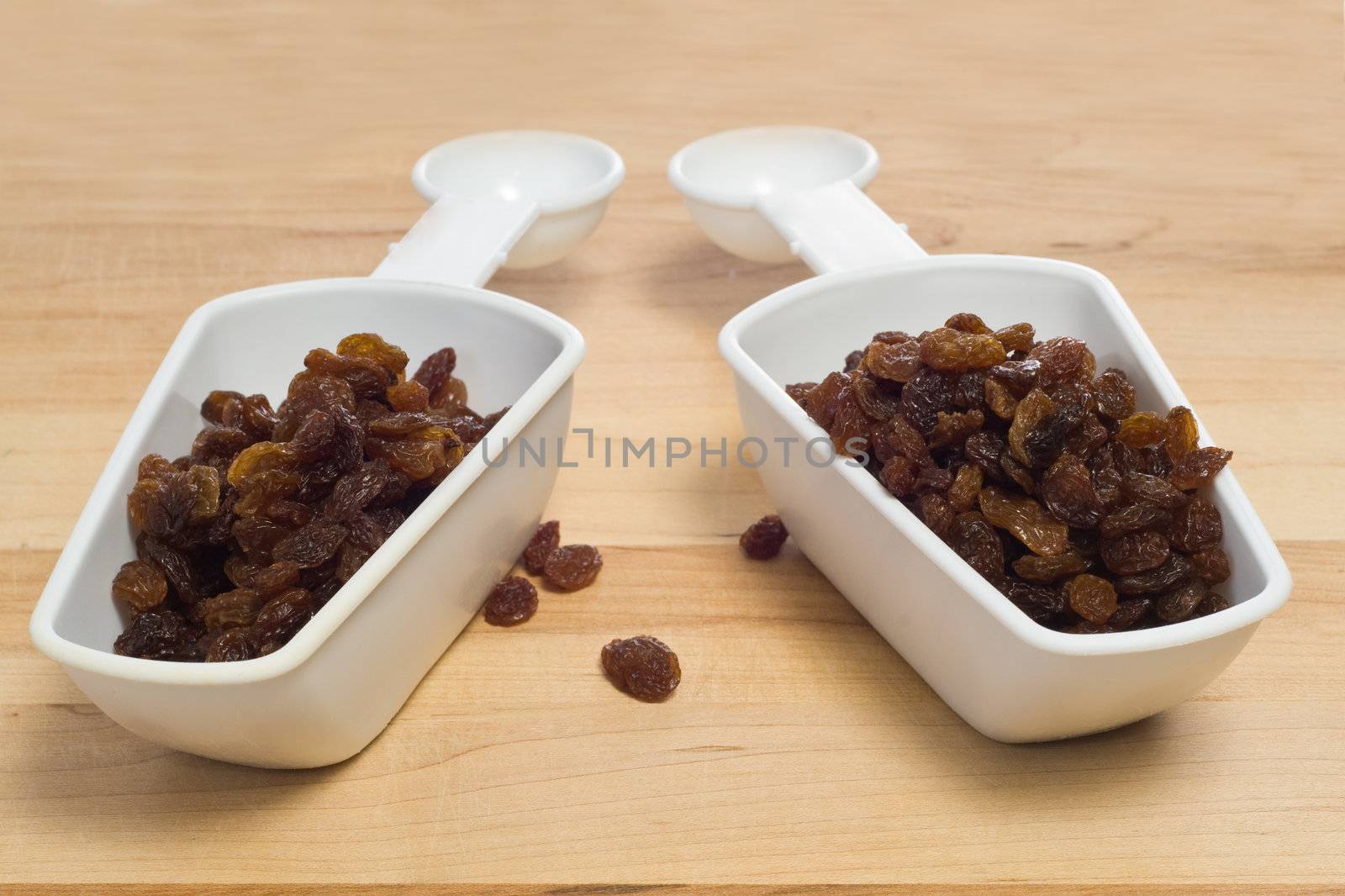 Two measuring cups full of raisins, shot on a wooden board