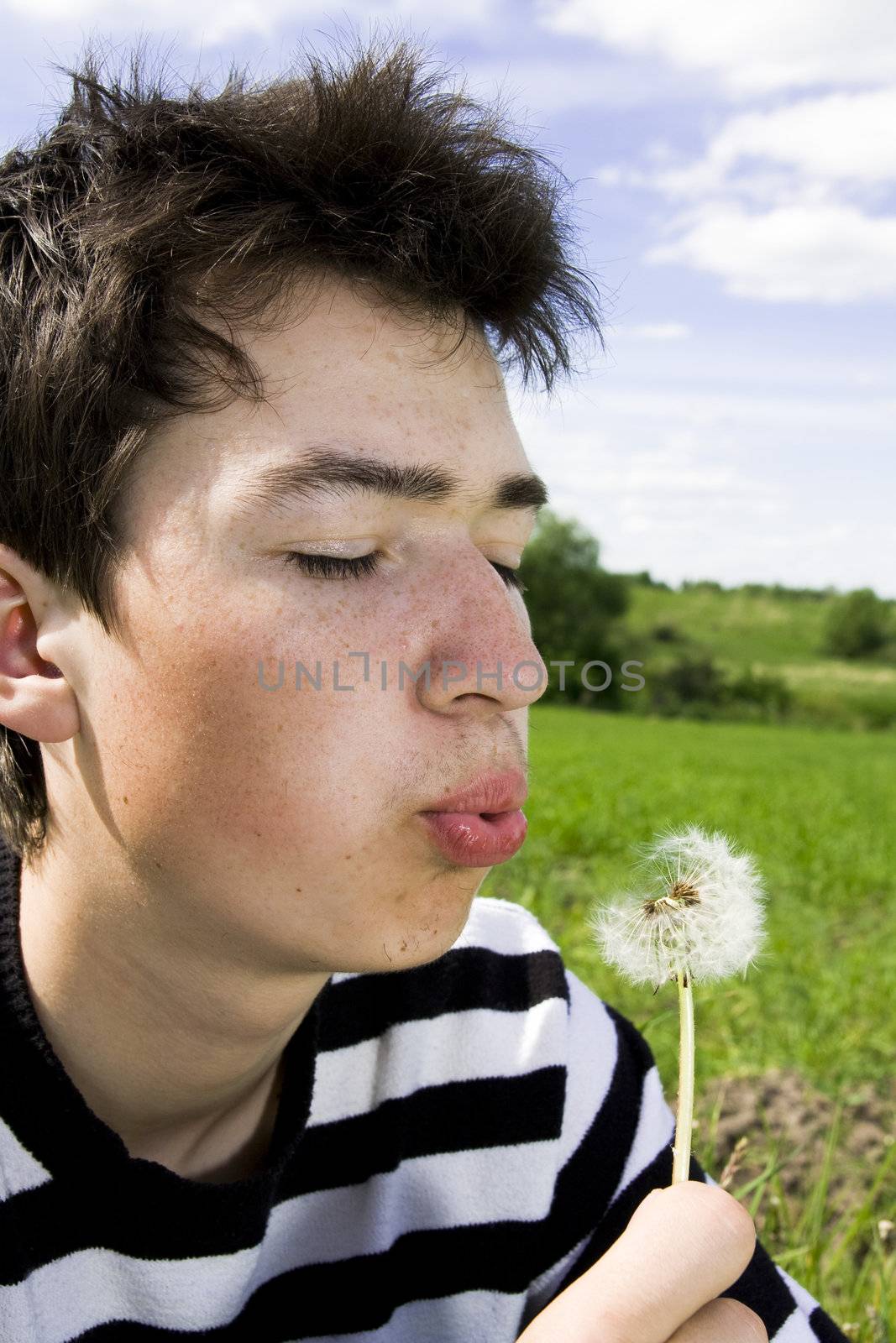 Young teenager blowing dandelion at sunny day
