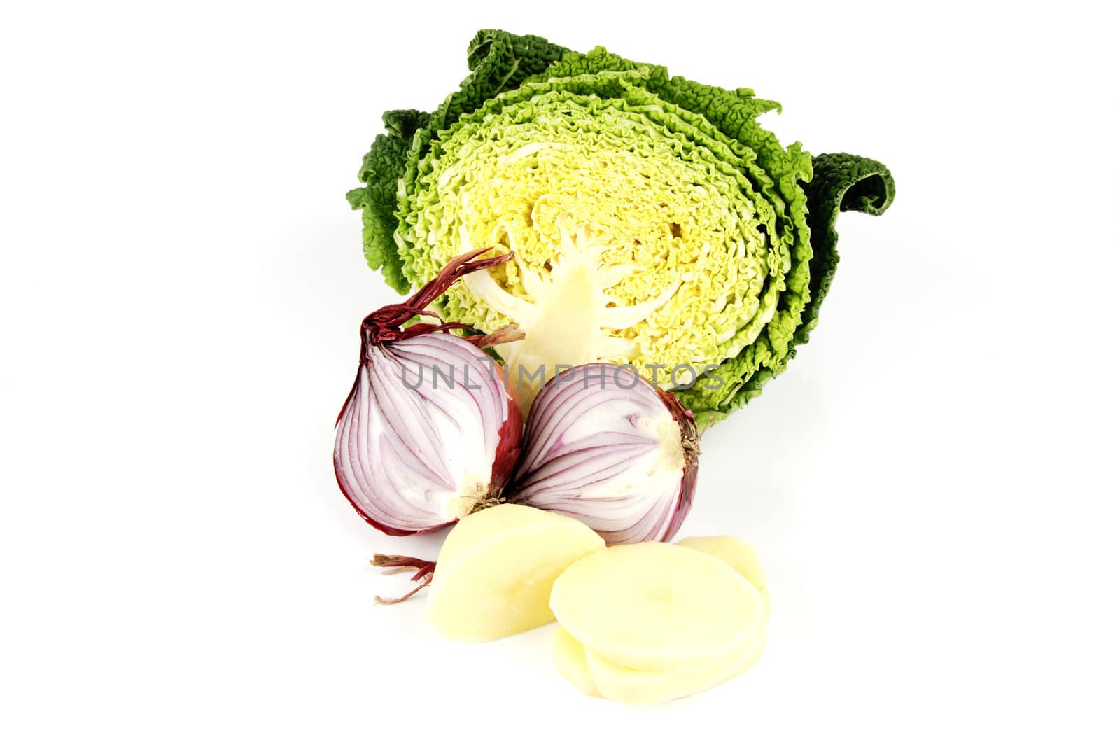 Half a raw green cabbage with a red onion cut in half and peeled potato slices on a reflective white background