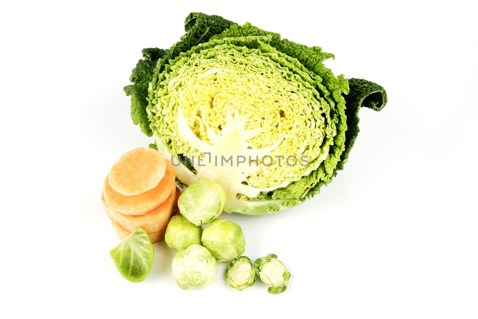 Half a raw green cabbage with slices of raw sweet potato and peeled green sprouts on a reflective white background