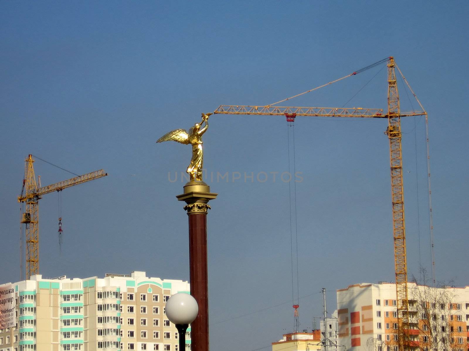 Gold statue reaches the crane on a background of new houses