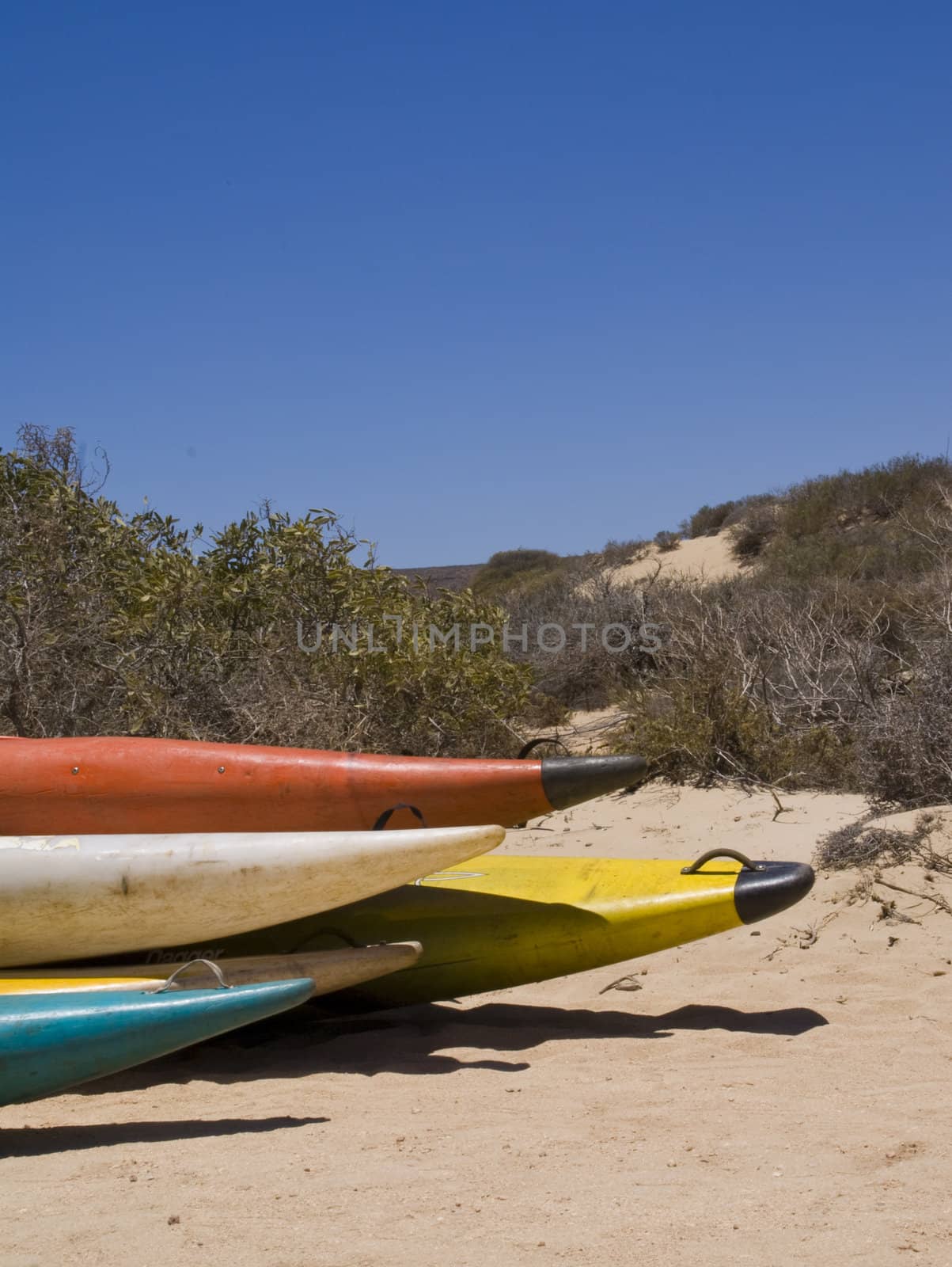 A colorful stack of canoes in the dunes under a bright sky.