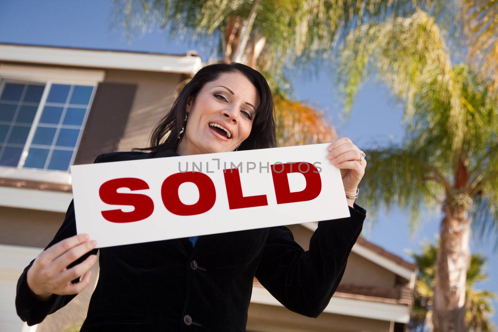 Happy Attractive Hispanic Woman Holding Sold Sign In Front of House.