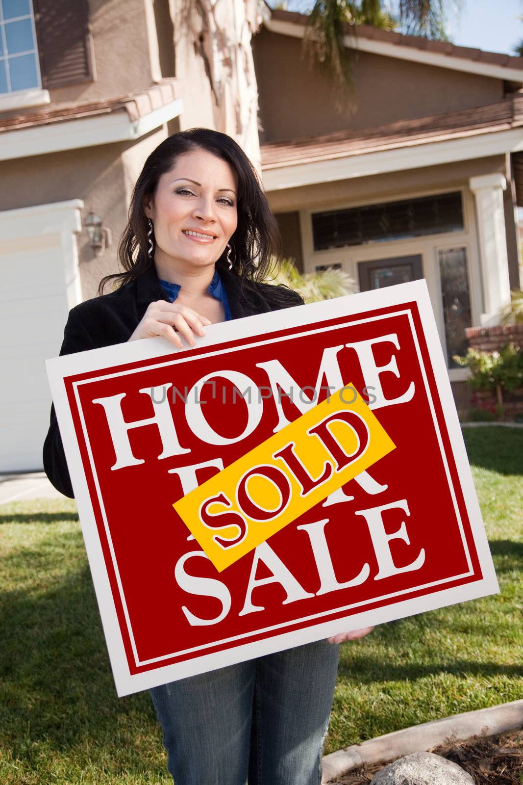 Happy Attractive Hispanic Woman Holding Red Sold Home For Sale Sign In Front of House.