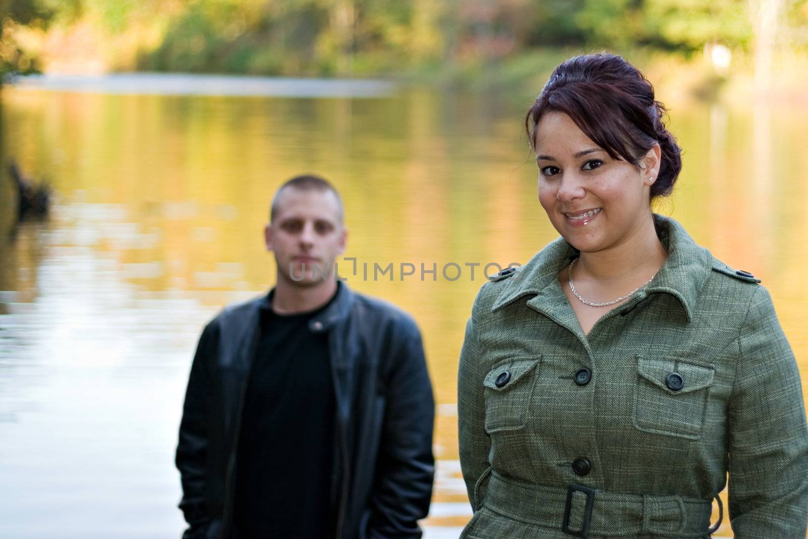 A young happy couple standing by a lake in autumn.  Shallow depth of field with focus on the woman.